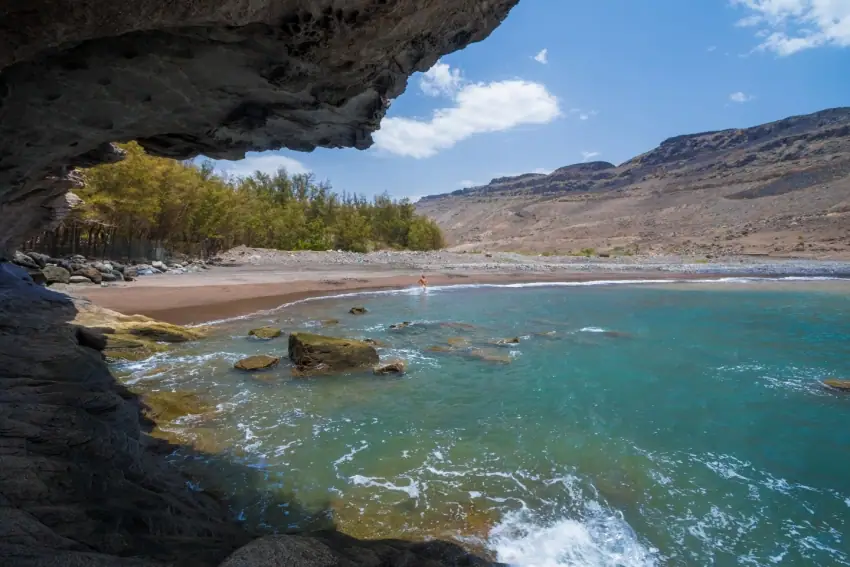 Naturstrand Veneguera mit dunklem Sand und Felsen