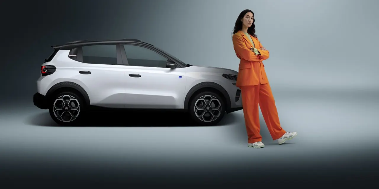 White SUV in a studio, a woman in an orange suit standing beside it